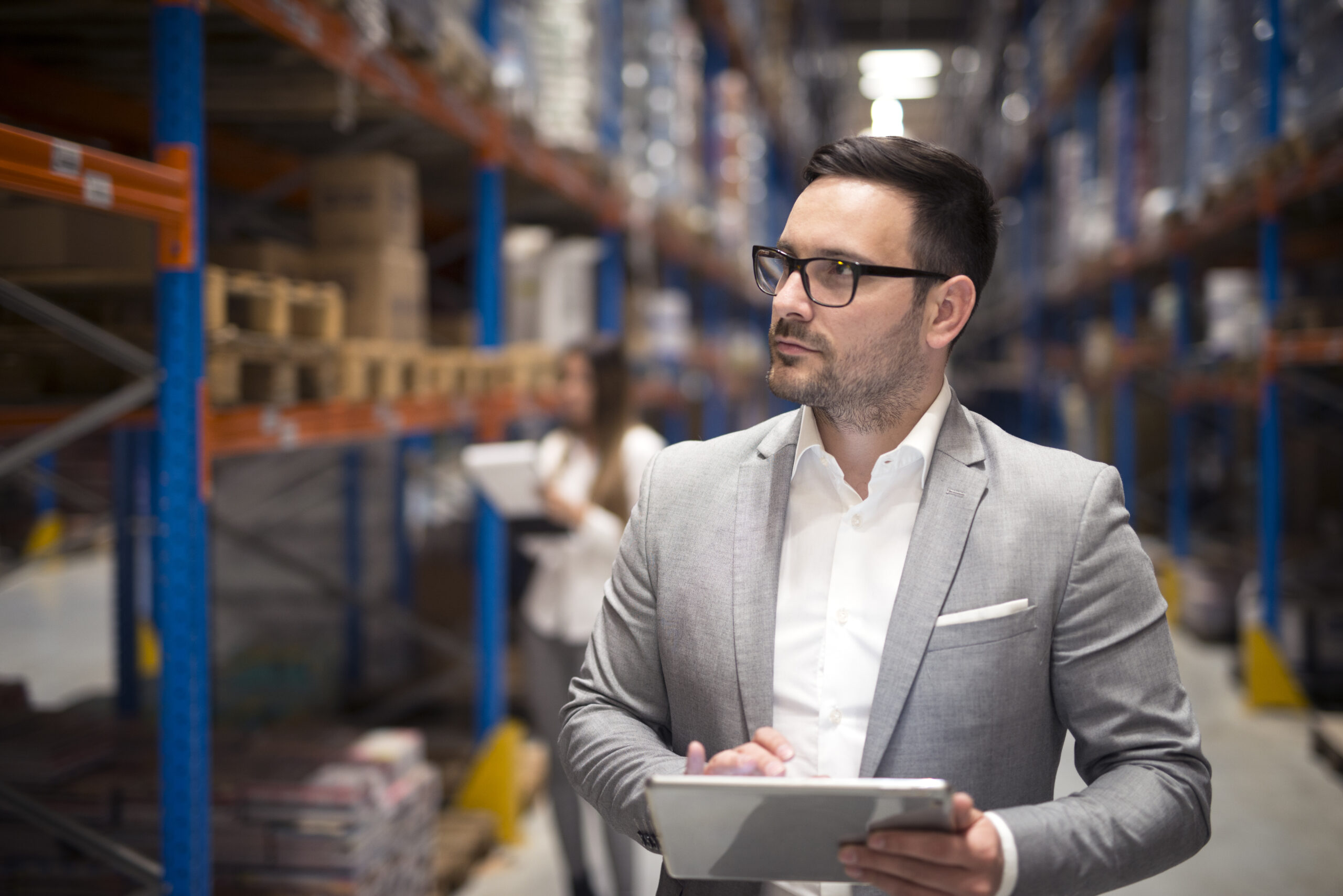 Home portrait successful businessman manager ceo holding tablet walking through warehouse storage area looking towards shelves scaled.jpg